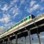 A sleek train crossing a historic bridge against a vibrant blue sky.