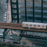 A drone captures a city train traveling on an elevated track amidst urban streets and buildings.
